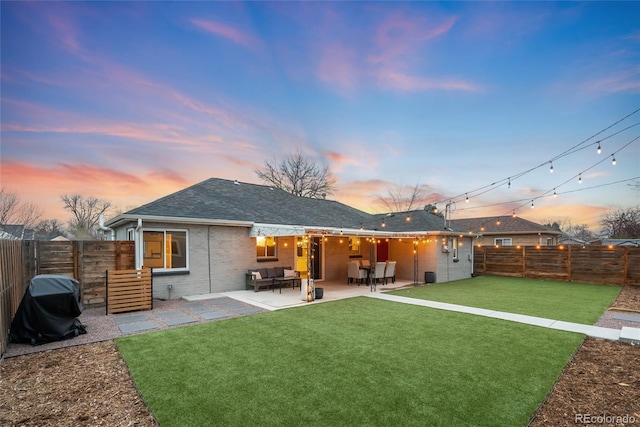 back of house at dusk with a fenced backyard, brick siding, a yard, and a patio area