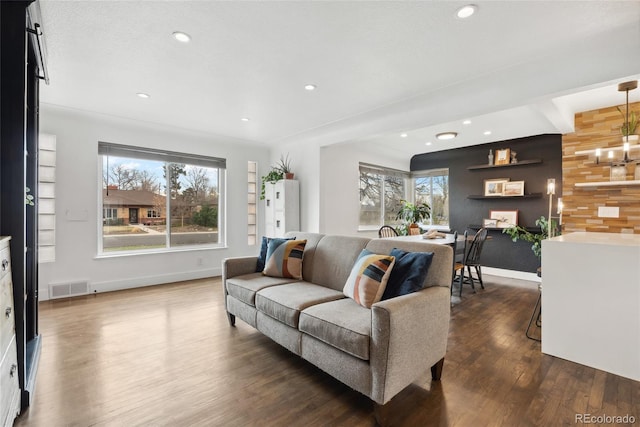 living area with dark wood-type flooring, visible vents, a healthy amount of sunlight, and wooden walls