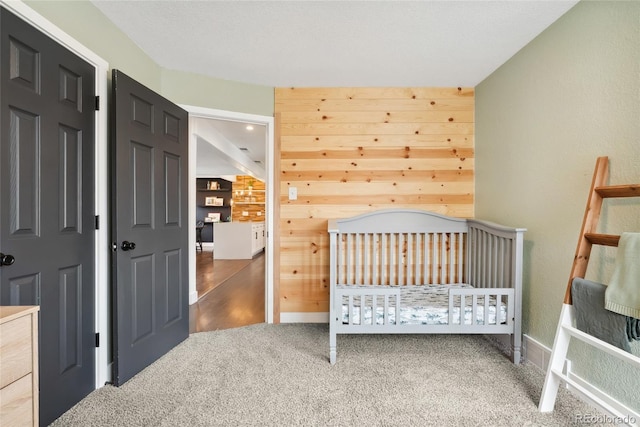 carpeted bedroom featuring a crib and wood walls