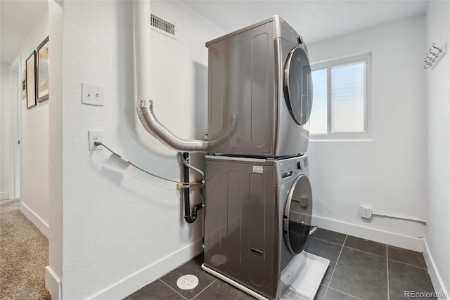 clothes washing area with laundry area, dark tile patterned flooring, baseboards, and stacked washing maching and dryer
