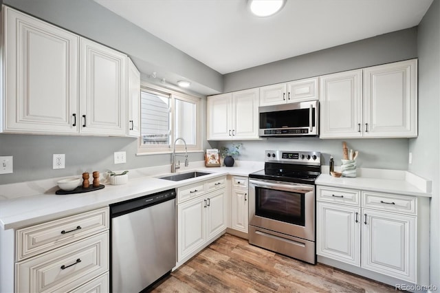 kitchen featuring stainless steel appliances, white cabinets, a sink, and light wood-style flooring