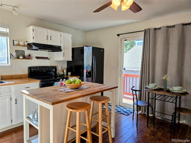 kitchen with a kitchen bar, black appliances, butcher block countertops, dark hardwood / wood-style flooring, and white cabinetry