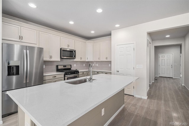 7285 S Titus Way, Aurora, CO 80016 - kitchen with stainless steel appliances, light wood finished floors, white cabinets, decorative backsplash, and an island with sink