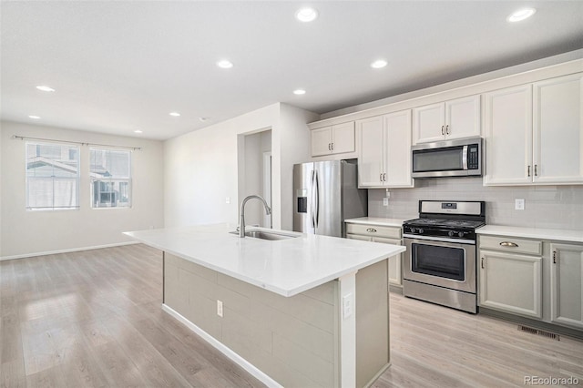 kitchen with stainless steel appliances, sink, light hardwood / wood-style flooring, white cabinets, and an island with sink