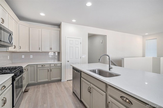 kitchen featuring sink, light hardwood / wood-style flooring, gray cabinets, appliances with stainless steel finishes, and tasteful backsplash