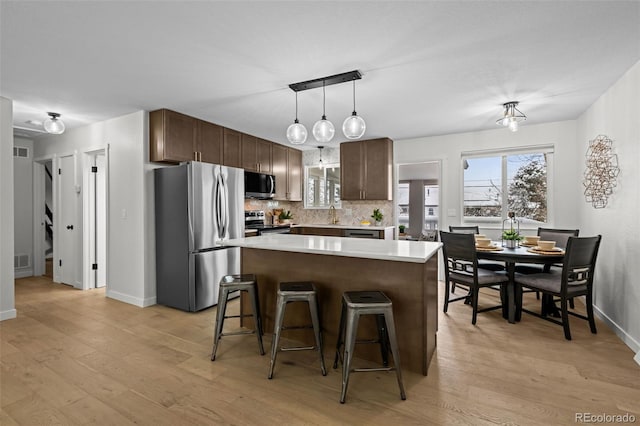 kitchen with a kitchen island, a breakfast bar, decorative backsplash, stainless steel appliances, and dark brown cabinets