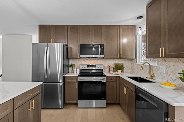 kitchen featuring stainless steel appliances, backsplash, hanging light fixtures, light stone counters, and sink