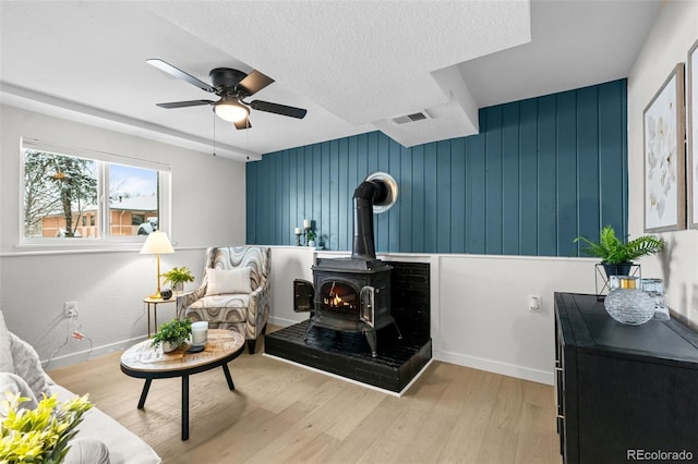 sitting room featuring hardwood / wood-style flooring, wooden walls, ceiling fan, a wood stove, and a textured ceiling