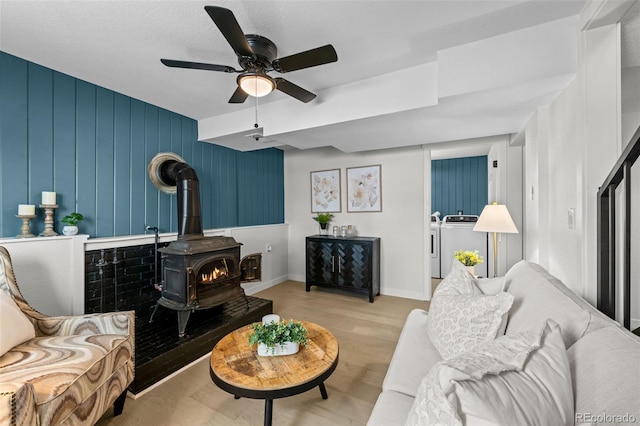 living room with ceiling fan, light hardwood / wood-style flooring, separate washer and dryer, a textured ceiling, and a wood stove