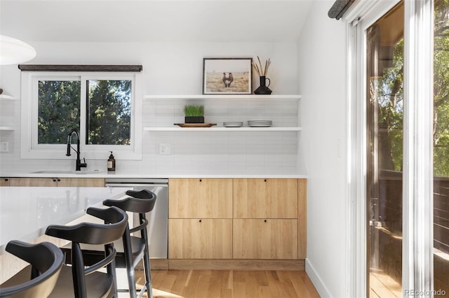 bar featuring light brown cabinetry, a healthy amount of sunlight, sink, dishwasher, and light hardwood / wood-style floors