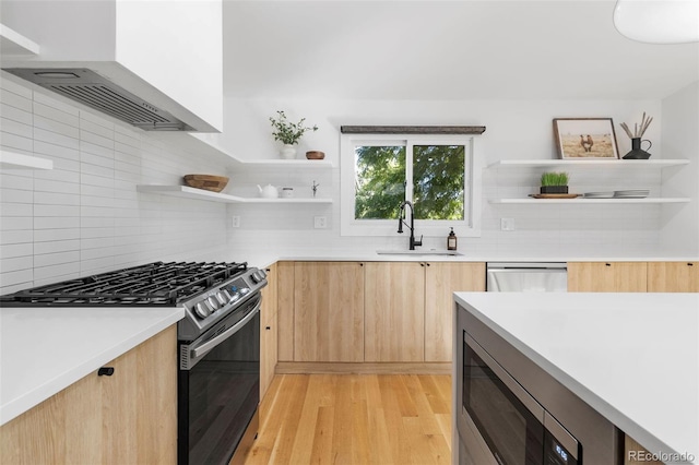 kitchen featuring light brown cabinets, wall chimney range hood, sink, light hardwood / wood-style floors, and stainless steel appliances