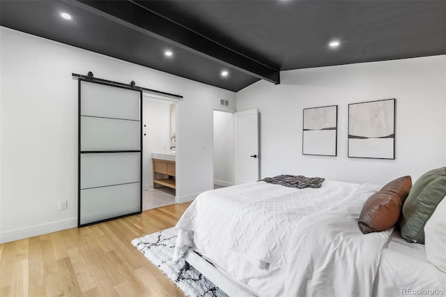 bedroom featuring connected bathroom, a barn door, vaulted ceiling with beams, and light wood-type flooring