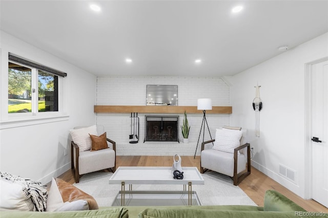 living room with a fireplace, brick wall, and light hardwood / wood-style flooring