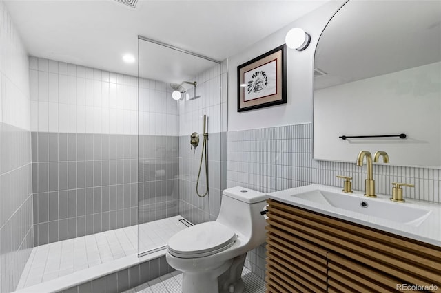 bathroom with tile patterned floors, vanity, tiled shower, tile walls, and toilet