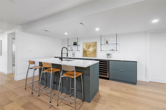 kitchen with a center island with sink, beverage cooler, light wood-type flooring, and sink