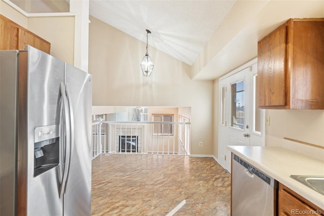 kitchen featuring a textured ceiling, hanging light fixtures, a tile fireplace, lofted ceiling, and appliances with stainless steel finishes