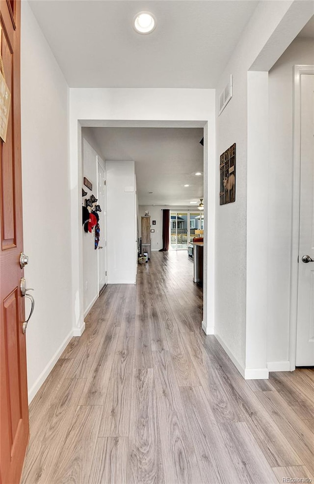 hall featuring light wood finished floors, baseboards, and visible vents