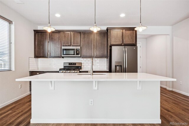 kitchen with an island with sink, appliances with stainless steel finishes, and hanging light fixtures