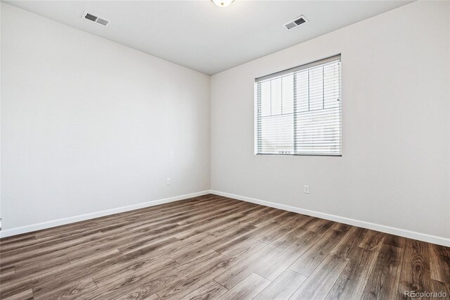 unfurnished room featuring dark wood-style flooring, visible vents, and baseboards