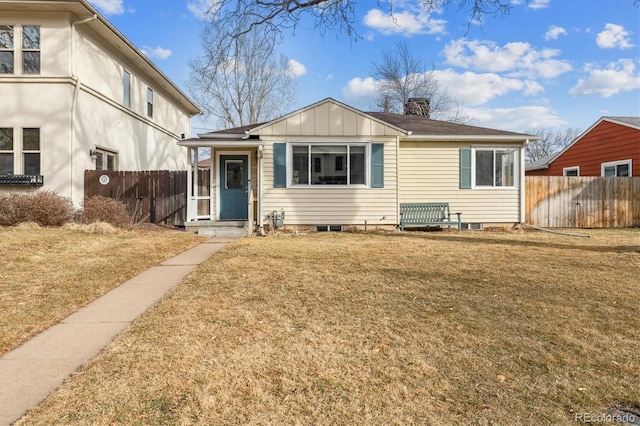 view of front facade featuring a chimney, board and batten siding, a front yard, and fence