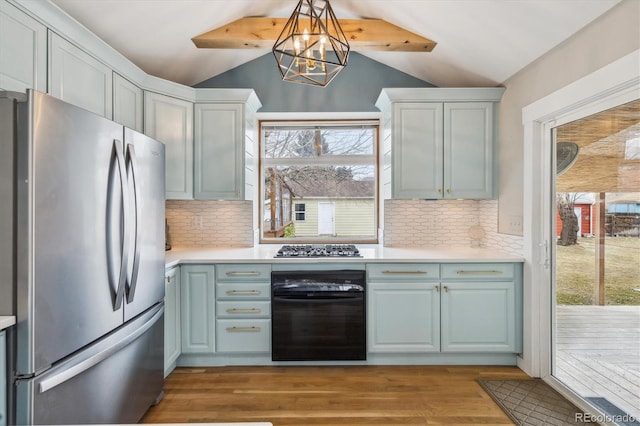 kitchen featuring pendant lighting, appliances with stainless steel finishes, light hardwood / wood-style floors, decorative backsplash, and vaulted ceiling