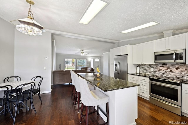 kitchen featuring appliances with stainless steel finishes, a kitchen island, white cabinetry, decorative light fixtures, and dark hardwood / wood-style floors