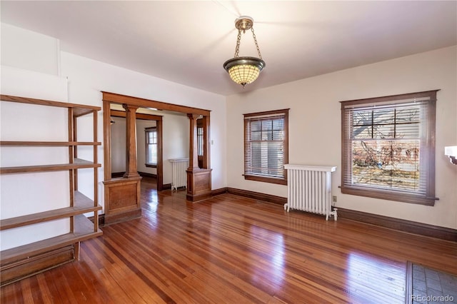 unfurnished room featuring ornate columns, dark hardwood / wood-style flooring, and radiator heating unit