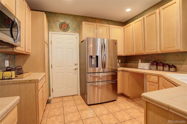 kitchen with appliances with stainless steel finishes, light brown cabinetry, sink, light tile patterned floors, and tile counters