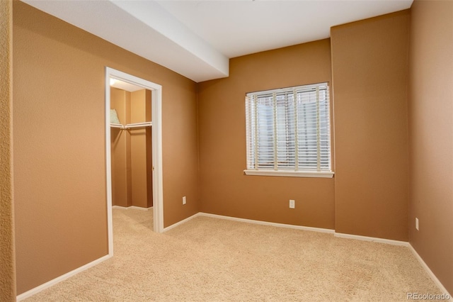 unfurnished bedroom with a walk in closet, light carpet, and a closet