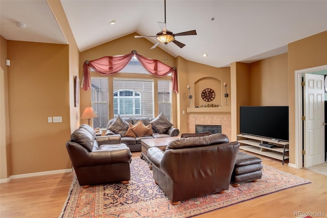 living area with a ceiling fan, light wood-type flooring, a tiled fireplace, lofted ceiling, and baseboards