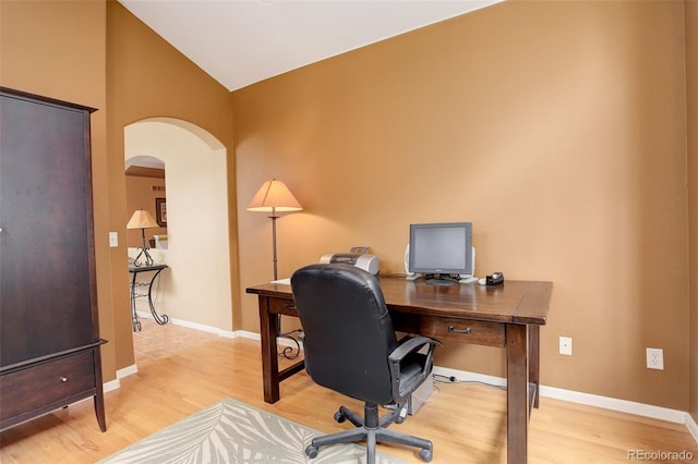 home office with arched walkways, light wood-style flooring, baseboards, and vaulted ceiling