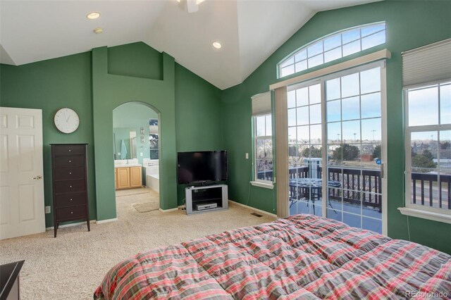 carpeted bedroom featuring high vaulted ceiling, multiple windows, arched walkways, and ensuite bath