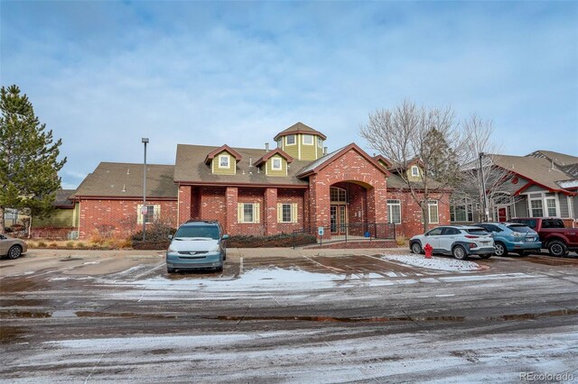 view of front of house with brick siding, uncovered parking, and roof with shingles