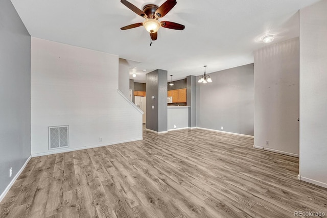 unfurnished living room featuring light wood-style flooring, ceiling fan with notable chandelier, visible vents, and baseboards