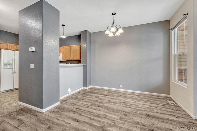 unfurnished dining area featuring light wood finished floors, baseboards, and an inviting chandelier