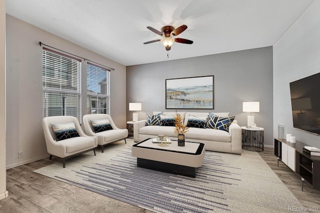 living area with baseboards, ceiling fan, and wood finished floors