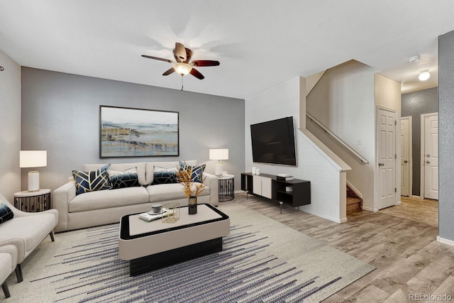 living area with stairway, baseboards, a ceiling fan, and wood finished floors