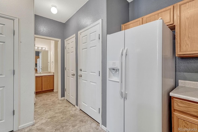 kitchen featuring baseboards, white refrigerator with ice dispenser, light countertops, and a textured wall