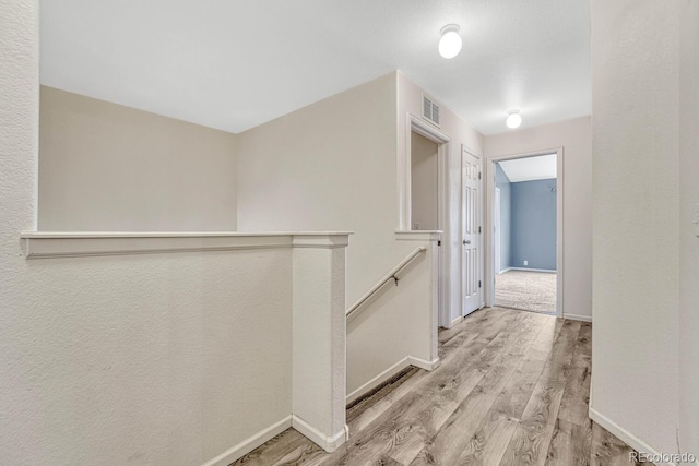 hall featuring an upstairs landing, visible vents, baseboards, and wood finished floors