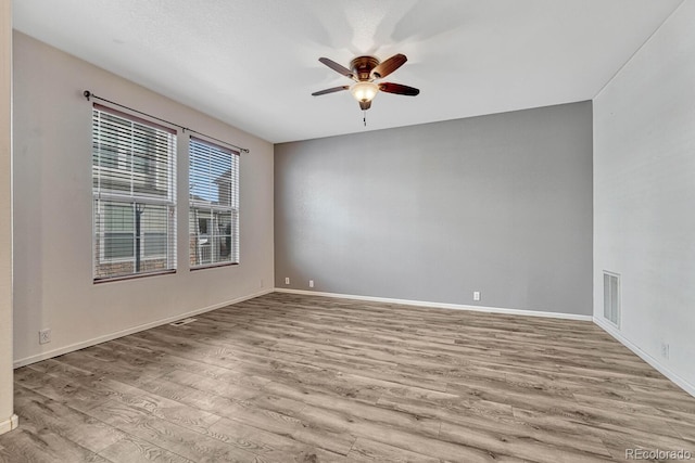 spare room featuring baseboards, wood finished floors, visible vents, and ceiling fan