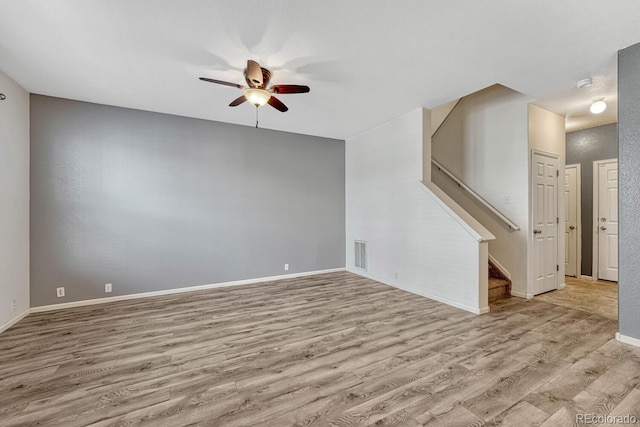 unfurnished living room featuring visible vents, baseboards, stairway, wood finished floors, and a ceiling fan