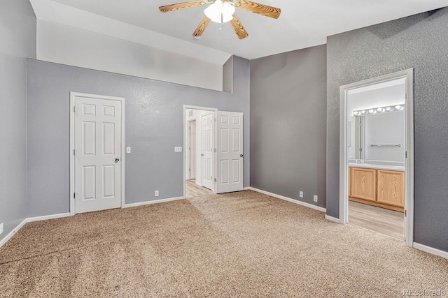 unfurnished bedroom featuring a ceiling fan, baseboards, lofted ceiling, ensuite bathroom, and light carpet