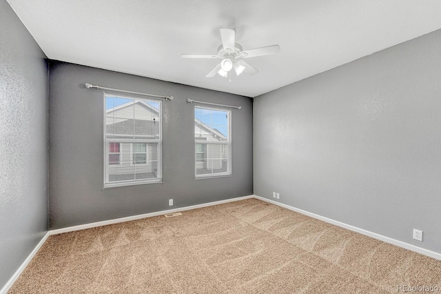 carpeted spare room with visible vents, baseboards, ceiling fan, and a textured wall