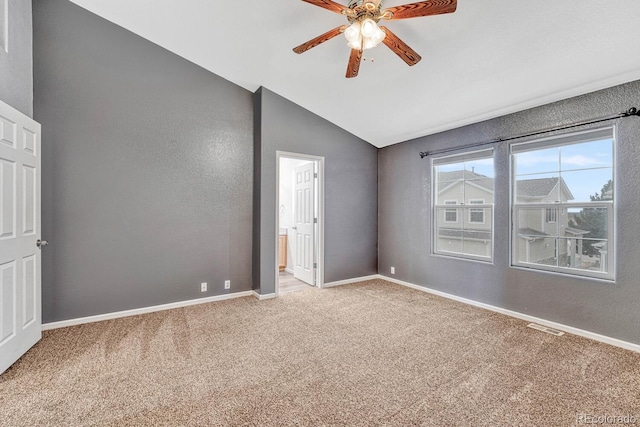 unfurnished bedroom with visible vents, baseboards, light colored carpet, lofted ceiling, and ensuite bath