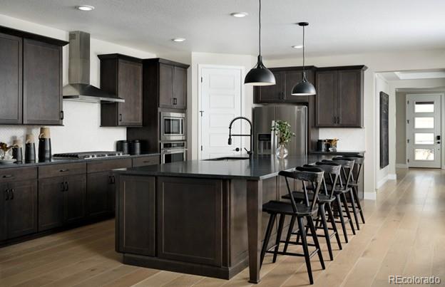 4125 N Duquesne Ct, Aurora, CO 80019 - kitchen featuring wall chimney range hood, appliances with stainless steel finishes, dark countertops, a breakfast bar, and recessed lighting