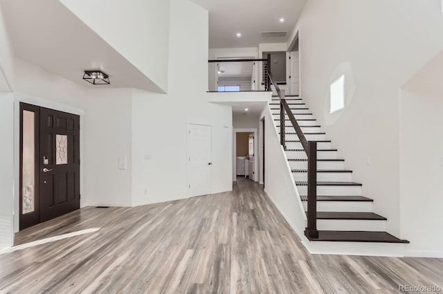 entryway featuring a wealth of natural light, a towering ceiling, and light hardwood / wood-style flooring