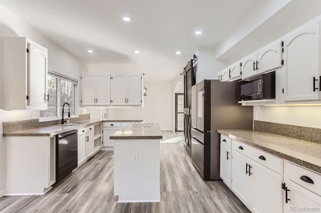 kitchen featuring black appliances, a barn door, sink, light hardwood / wood-style floors, and a center island