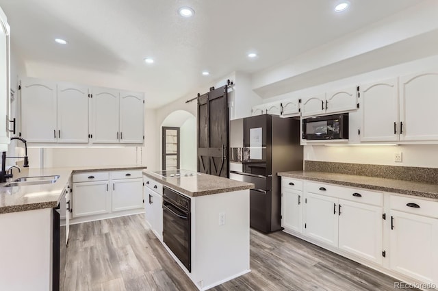 kitchen with a barn door, white cabinetry, sink, and black appliances