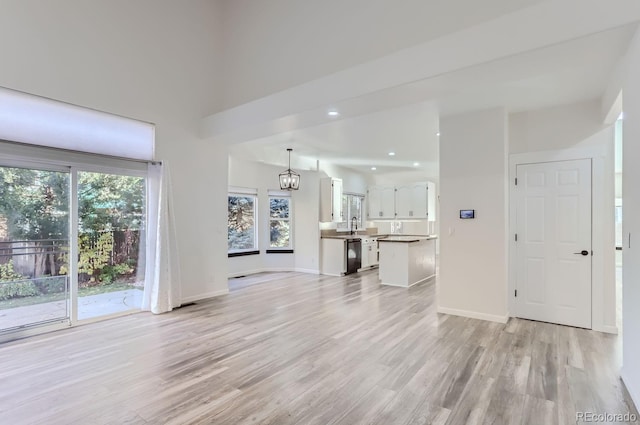 unfurnished living room with an inviting chandelier, sink, and light hardwood / wood-style flooring