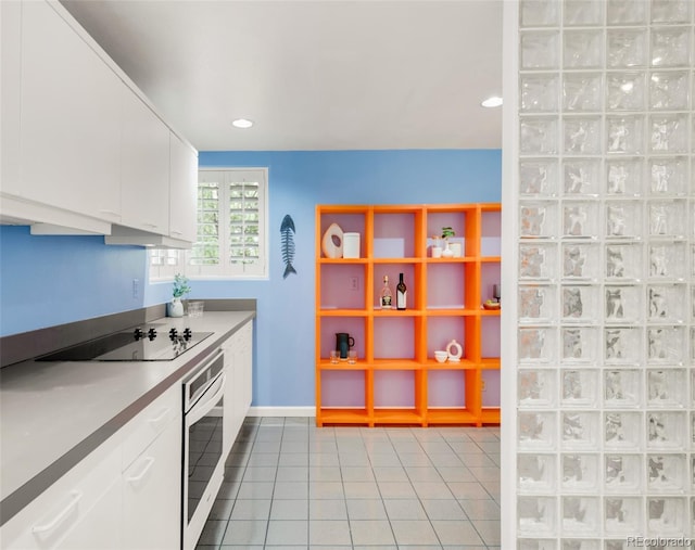 kitchen with black electric stovetop, white cabinetry, white oven, baseboards, and light tile patterned floors